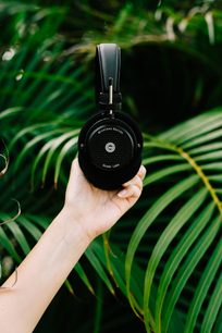 Sort Grado GW100 hovedtelefoner holdt i en hånd foran friske grønne palmeblade