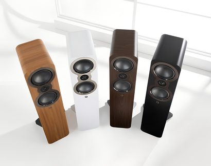 Top-down view of four floorstanding speakers in light wood, white, dark wood, and black finishes, with matte-surfaced MDF cabinets that are either veneered or painted, rounded fronts housing two stacked circular drivers flanking a central tweeter, all set on rectangular bases
