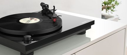Svart platespiller plassert på et hvitt møbel, sett ovenfra, med en vinylplate på