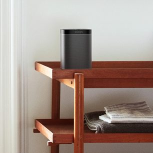 Sonos One (Gen 2) mat sort højttaler på træhylde, hvid sammenfoldet serviet ved siden af, tæt forfra-udsigt