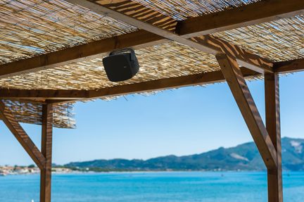 Cassa da esterno nera fissata sotto una pergola in legno con tetto in cannicciato di fronte al mare