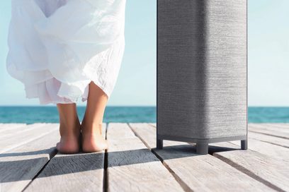 Kvindelige bare fødder på træterrasse, foran hvidt gardin og grå lampefod, ved strandkanten
