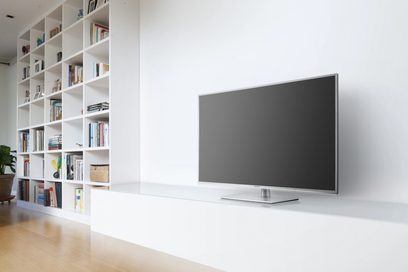 Fladskærms-tv stående på et hvidt møbel foran en hvid vægbogreol fyldt med bøger