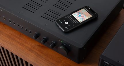 Czarny wzmacniacz hi-fi widziany pod kątem trzech czwartych, przyciski na panelu przednim i smartfon z odtwarzaczem muzyki na górze