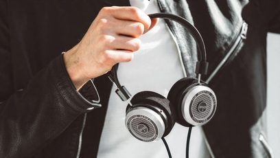 Offener Hi-Fi-Kopfhörer Grado SR325x, von einer Männerhand gehalten, in linker Seitenansicht, vor schwarzem Hintergrund