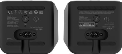 Двойка свързани високоговорители Klipsch Flexus Surr 200, компактни кутии от мат черен пластик, заден изглед, показващ буквите ляво-дясно, кръгло бутонче за свързване и вграден порт за захранване