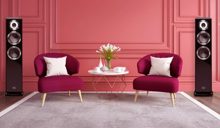 To fuchsia lænestole med hvide puder, hvidt rundt sofabord, hvid vase med blomster, to sorte højttalere, lyserød væg