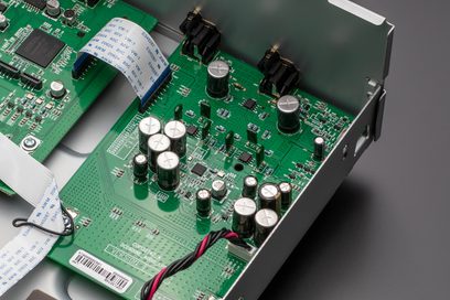 Vihreä piirilevy elektronisine komponentteineen, kondensaattoreineen ja mustavalkoisine liittimineen, lähikuva Denon DCD-900NE -hopeisen CD-soittimen sisältä