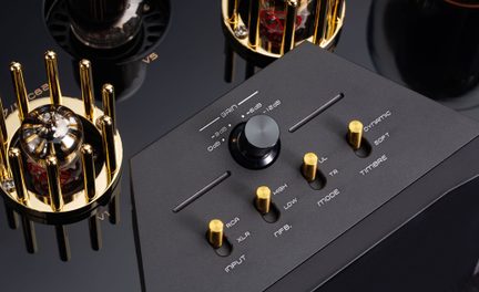 Pannello di controllo di amplificatore valvolare, metallo nero opaco, manopole dorate, valvole sotto gabbie dorate, primo piano obliquo