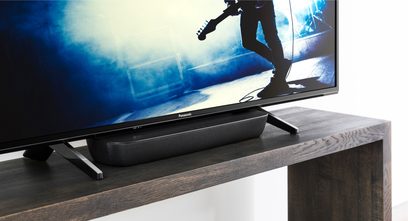 Sort Panasonic SC-HTB250EGK soundbar under et fladskærms-TV, der viser en guitarist, set forfra i let nedadgående vinkel