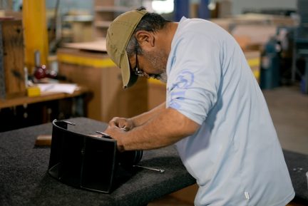 Man assembling a black compartmentalized bag on a workbench in a workshop