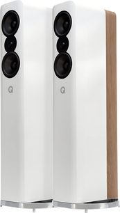 Pár sloupových reproduktorů Q Acoustics Concept 500 v bílém laku, bílá lesklá skříň s světlými dřevěnými boky, přední panel se třemi černými kruhovými reproduktory a diskrétním logem, umístěné na kovovém podstavci, pohled ze tří čtvrtin