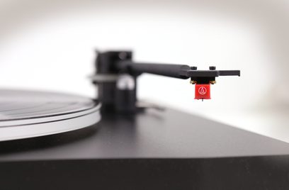 Tonarm til vinylpladespiller med rød pickup på sort vinylplade, tæt nærbillede i profil