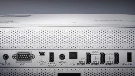 Bagsiden af en sølvfarvet hjemmebiografforstærker med HDMI-stik, USB-porte og lydindgange, perforeret ventilationsgitter