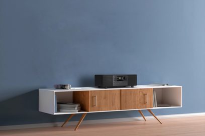 Mobile TV in legno chiaro con due scomparti aperti e uno scomparto chiuso, su piedini in metallo, con un sistema audio nero posizionato sopra