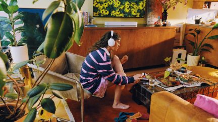 Hvidt Sony WH-1000XM5 trådløst headset båret af en kvinde i en farverig stue