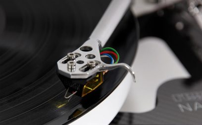 Hi-fi pladespiller Rega Naia med Aphelion 2 MC pickup, nærbillede af den sølvfarvede tonearm og den sort-gule pickup