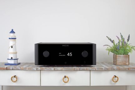 Sort, rektangulær forstærker med to cirkulære knapper, skærm der viser "XLR Analog Input 45", placeret på et træbord