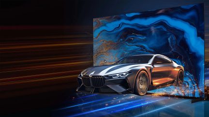 Sportovní auto v kovově šedé barvě zobrazené z předního tříčtvrtečního pohledu, lesklá kovová karoserie s širokou maskou chladiče, tenkými LED světlomety a širokými koly, vypadá, jako by vyjíždělo z obří obrazovky s abstraktními vzory v modré a zlaté barvě, světelné stopy a jiskry zdůrazňují pohyb.