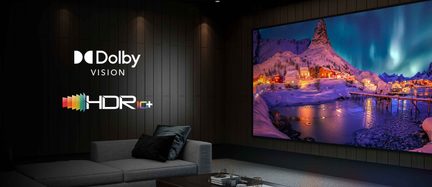 Un divano grigio con cuscini neri, uno schermo che mostra un paesaggio notturno innevato, loghi Dolby Vision e HDR10+ su una parete nera