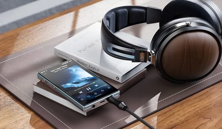 Cuffie audio circumaurali nere con finitura in legno collegate a un lettore Hi-Res appoggiato su dei libri