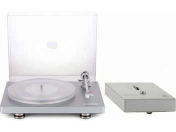 Sidabrinis vinilinių plokštelių grotuvas su atidarytu permatomu dangčiu ir tonarmu, šalia – „nano phono“ pirminis stiprintuvas