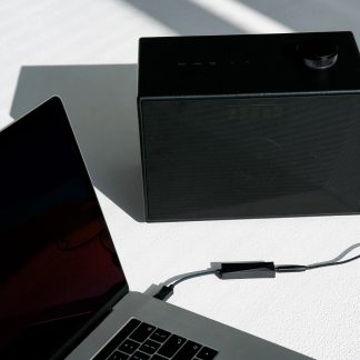 Sort højttaler, sort bærbar computer og kabel på hvid overflade, set ovenfra i nærbillede