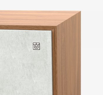 Tæt på-billede af hjørnet af en brun træramme med lys gråt tekstilpanel, lille firkantet metal-logo påsat