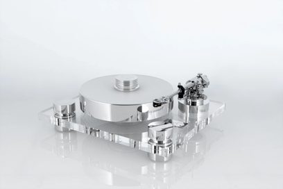Transrotor Bellini RB330 sølv hi-fi pladespiller, pladetallerken og tonearm i poleret metal monteret på en tyk, rektangulær sokkel i transparent akryl, set fra venstre forperspektiv