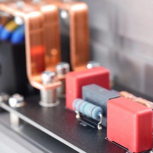 Tæt billede af indersiden af Inakustik AC-3200 Filter Digital SCHUKO-stikdåsen, kobberledende skinner, rektangulære røde plastkondensatorer, cylindrisk blå-grå modstand, sort printkort
