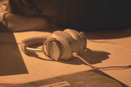Beige hovedtelefoner på tekstureret overflade, set fra siden, tykke puder, polstret bøjle, tilsluttet kabel, varm belysning