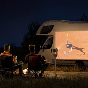 Videoproiettore XGIMI MoGo 3 Pro che proietta un'immagine di tennis sul lato di un camper, 2 persone sedute davanti a un fuoco