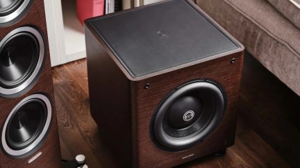 Subwoofer s povrchem z tmavého dřeva, velkým černým reproduktorem a čalouněnou matnou horní stranou
