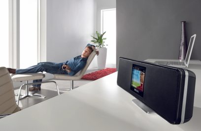 Philips NP2500 sort internetradio, set forfra, placeret på et hvidt bord, mand liggende på sofa i baggrunden