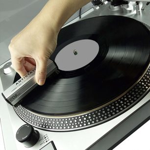 Pladespiller med sort tonarm, vinylplade og hånd, der holder en antistatisk Enova HIFI BVA 20 kulstofbørste