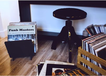 Sort pladespiller på træmøbel, brochure "Funk Masters", bøger og vinylplader stablet på træhylde