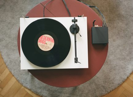 Tocadiscos de vinilo blanco visto desde arriba con disco negro y brazo de lectura sobre mesa redonda burdeos