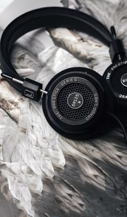 Åben hi-fi hovedtelefon Grado SR125x sort, set fra tre kvarter vinkel, liggende på hvide fjer, med sort opbevaringsetui