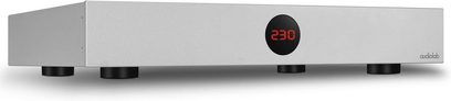 Τροφοδοτικό Audiolab DC-BLOCK 6 ασημί με κόκκινη ψηφιακή ένδειξη "230" στο κέντρο και μαύρα κυκλικά πόδια