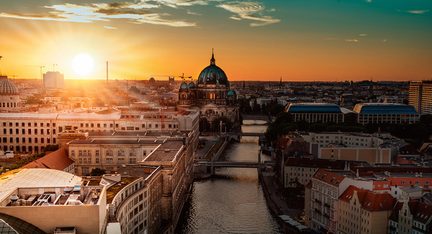 Vista aérea de Berlim ao pôr do sol, com a cúpula iluminada da catedral em primeiro plano, o rio Spree e os edifícios ao fundo
