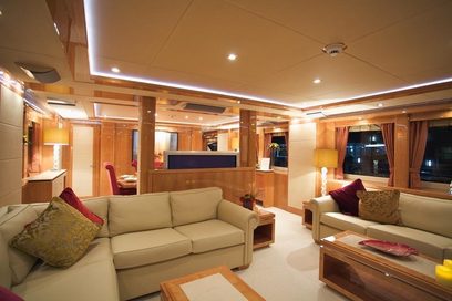 Luksuriøst yachtinteriør med beige sofaer, bordeauxrøde puder, træbordplader, indbygningsbelysning og vinduer