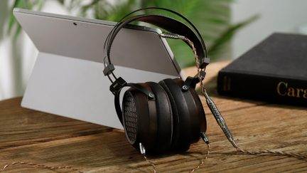 Brown over-ear hi-fi headphones with wooden earcups and a braided cable placed in front of a tablet on a wooden desk