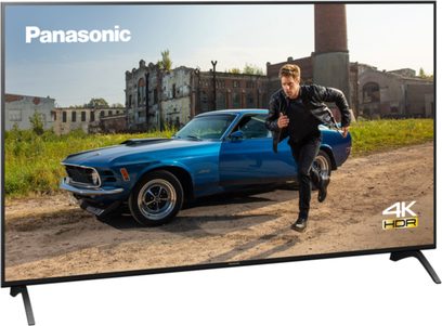 Televizor Panasonic TX-49HX940E 4K HDR zobrazující muže běžícího vedle modrého Fordu Mustang ze 70. let zaparkovaného před zchátralou budovou
