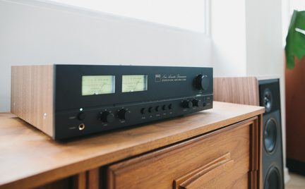 Svart forsterker med trefinér på sidene, to bakbelyste VU-metre, knapper og hodetelefonkontakt, visning i trekvart profil