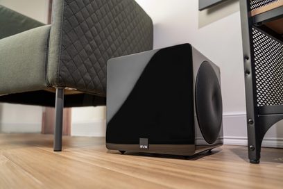 SVS 3000 Micro negru lucios subwoofer, văzut din față, așezat pe parchet, cu un fotoliu în fundal