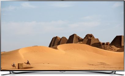 Sandpyramider i en ørken, en kamel og dens rytter i forgrunden, blå skyfri himmel
