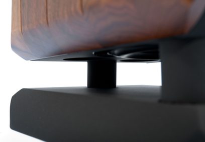 Chario Constellation Cygnus MK2 gulvhøjttaler i brun åretegnet træfinér, set nedefra ved samlingen mellem kabinet og sokkel med dæmpende cylinder og mat sort metalbase