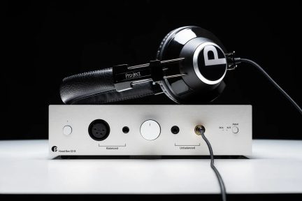 Wzmacniacz słuchawkowy Pro-Ject Head Box S3 B srebrny z położonym na nim czarnym zestawem słuchawkowym, widok z przodu na czarnym tle