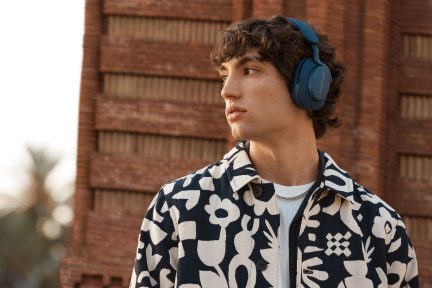Giovane uomo che indossa un paio di cuffie blu e una camicia a fantasia floreale nera e bianca, con uno sguardo pensieroso rivolto lontano