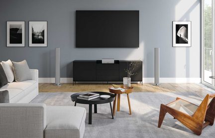 Šiuolaikinis šviesus salonas su pilka sofa, juodu TV staliuku, dideliu sieniniu ekranu ir stilingu mediniu foteliu